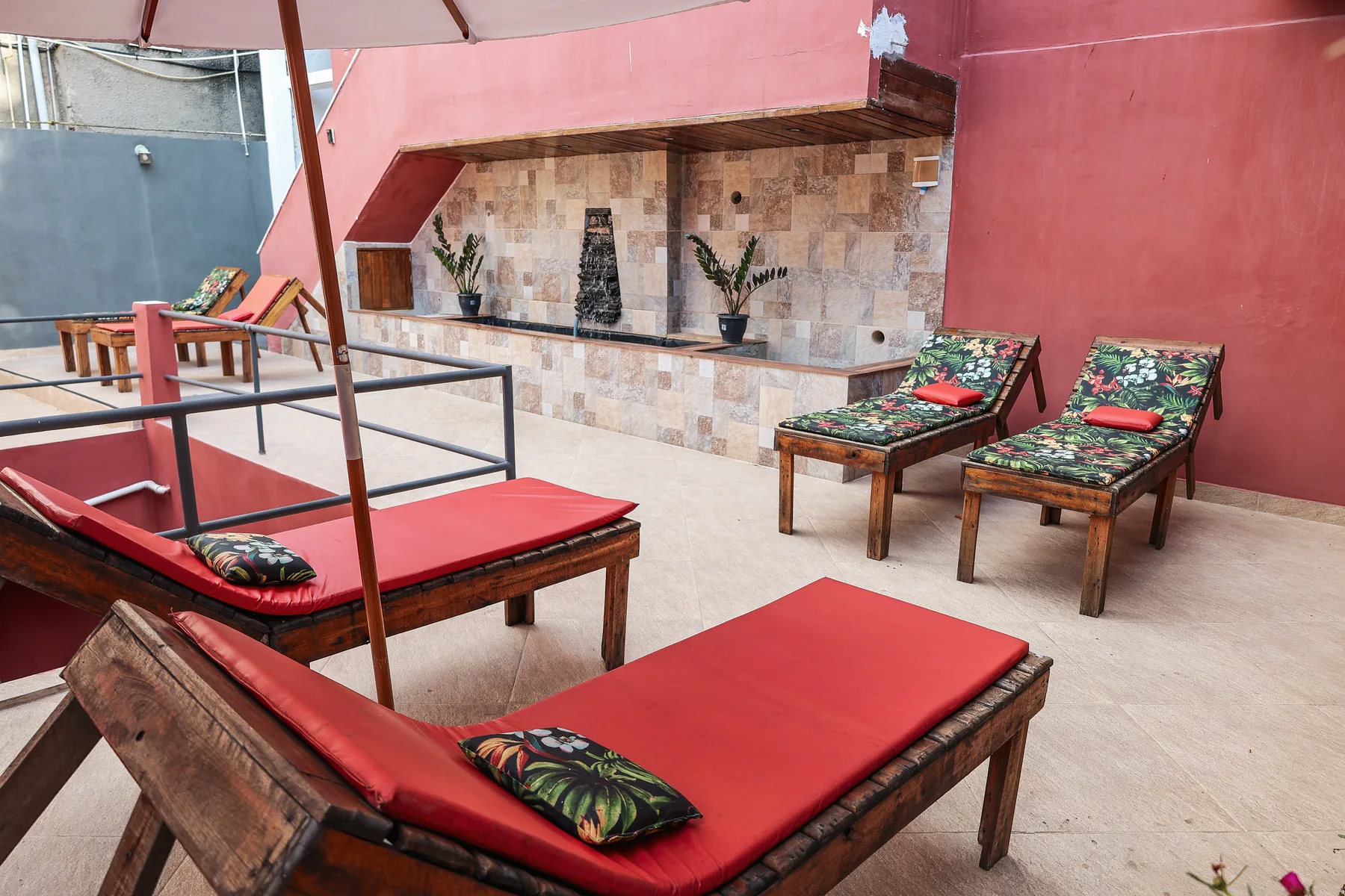 Pátio da Villa Dourada com espreguiçadeiras, guarda-sol e parede de pedra