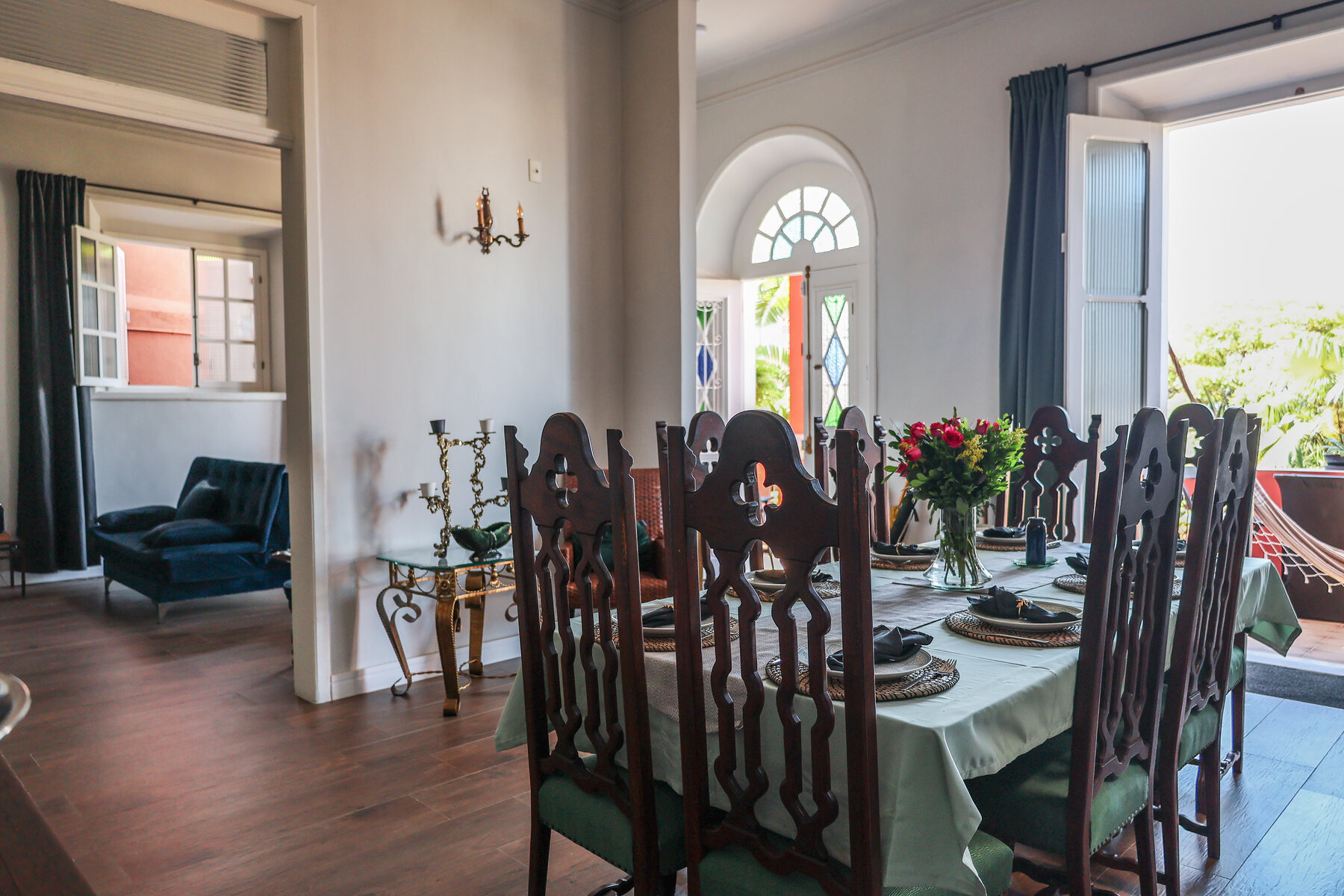 Sala de jantar da Villa Dourada com mesa posta, cadeiras históricas e acesso à varanda